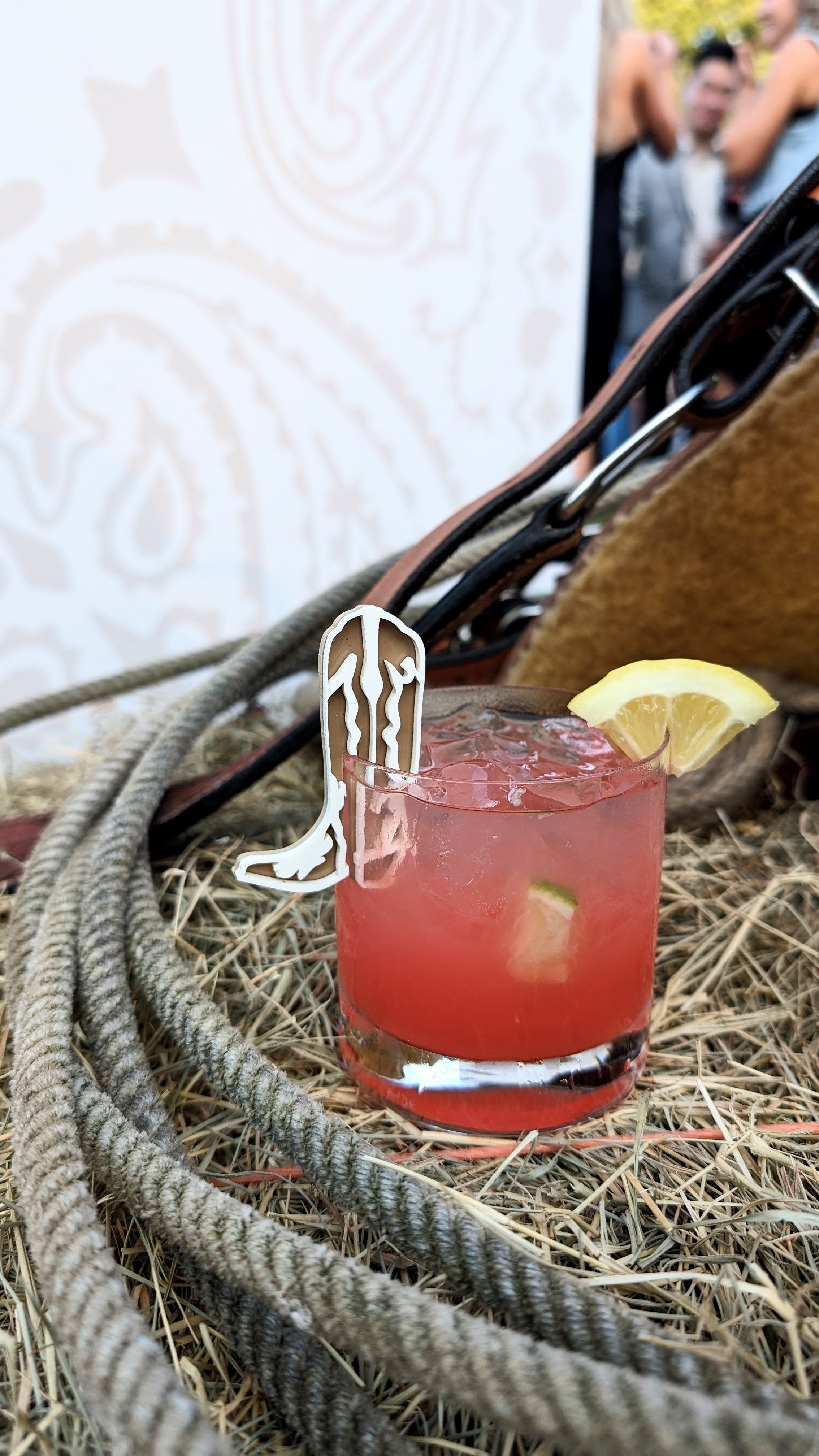 AALVO custom event detail. A red cocktail with a lemon slice on the side, garnished with a cowboy drink charm.
