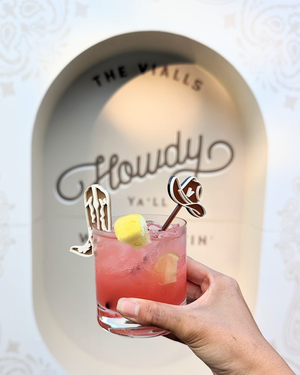 AALVO custom event details. Hand holding a pink cocktail with custom decorative drink stirrers in the shape of a cowboy hat and cowboy boots. 