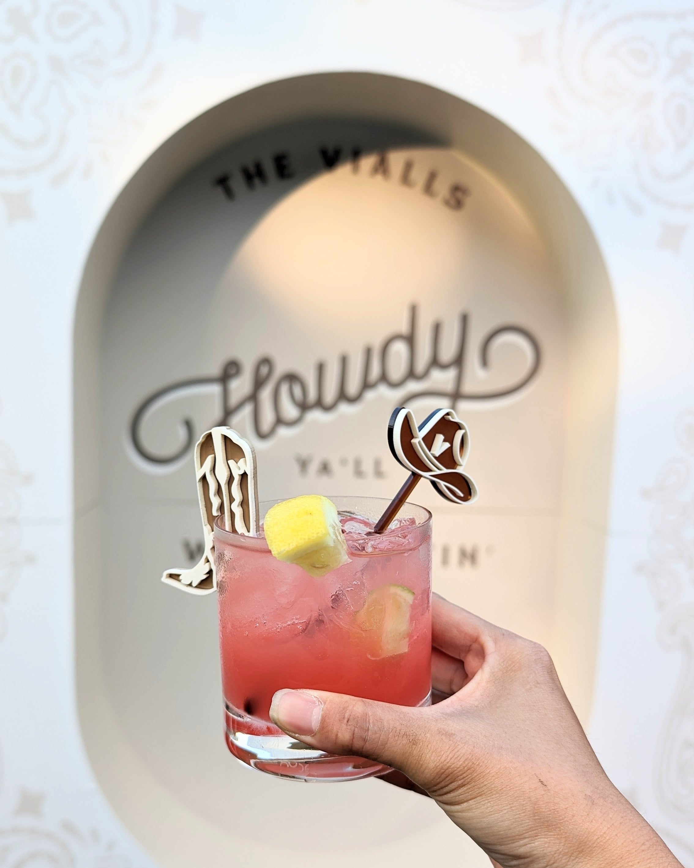 AALVO custom event details. Hand holding a pink cocktail with custom decorative drink stirrers in the shape of a cowboy hat and cowboy boots. 