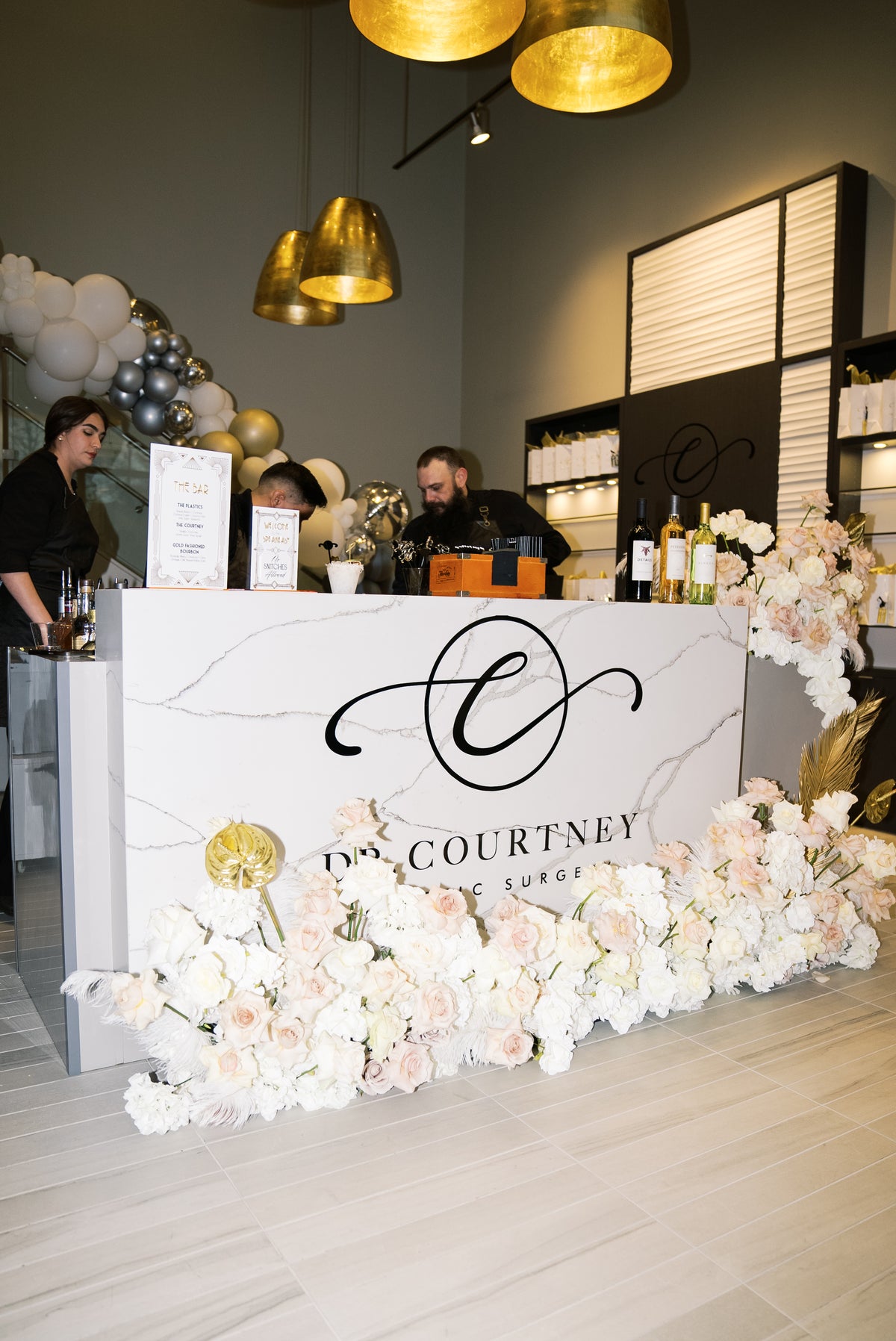 AALVO custom event signage. Marble reception counter sign with gold monogram for Dr. Courtney event, framed by white and blush floral garland.