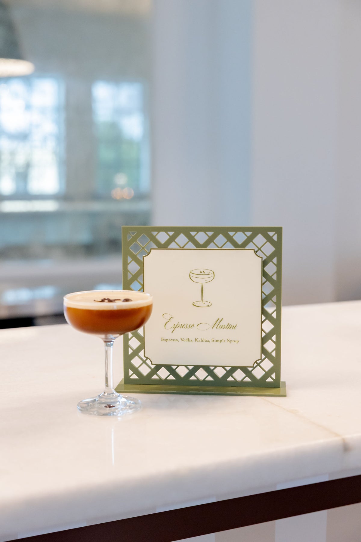 AALVO custom wedding signage. Sage green laser-cut espresso martini table sign beside a served espresso martini.